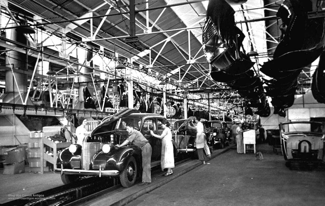Operários trabalhando em linha de produção de fábrica automotiva. Mulheres e homens trabalhando na funilaria e motor dos carros.